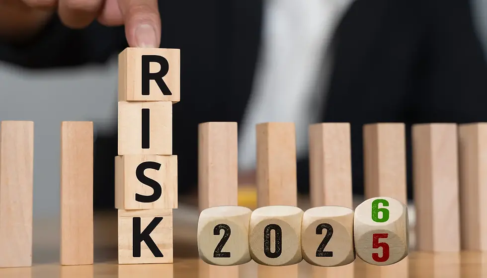 Finger stacking wooden blocks spelling "RISK"; A year on cubes with 2025 turning to 2026. Blurred office background.