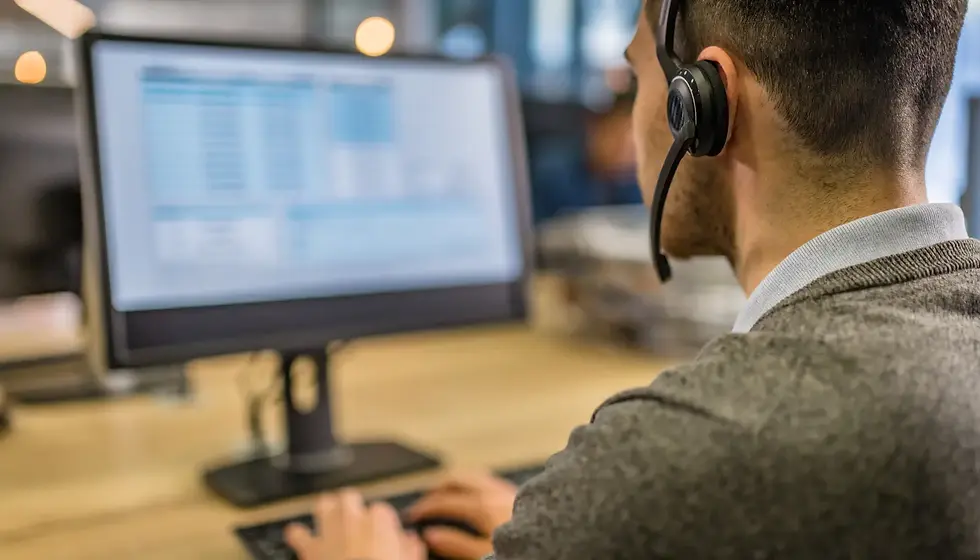 Man wearing headset works at a computer with blurred text on screen, in an office setting. Focus is on his back, conveying productivity.