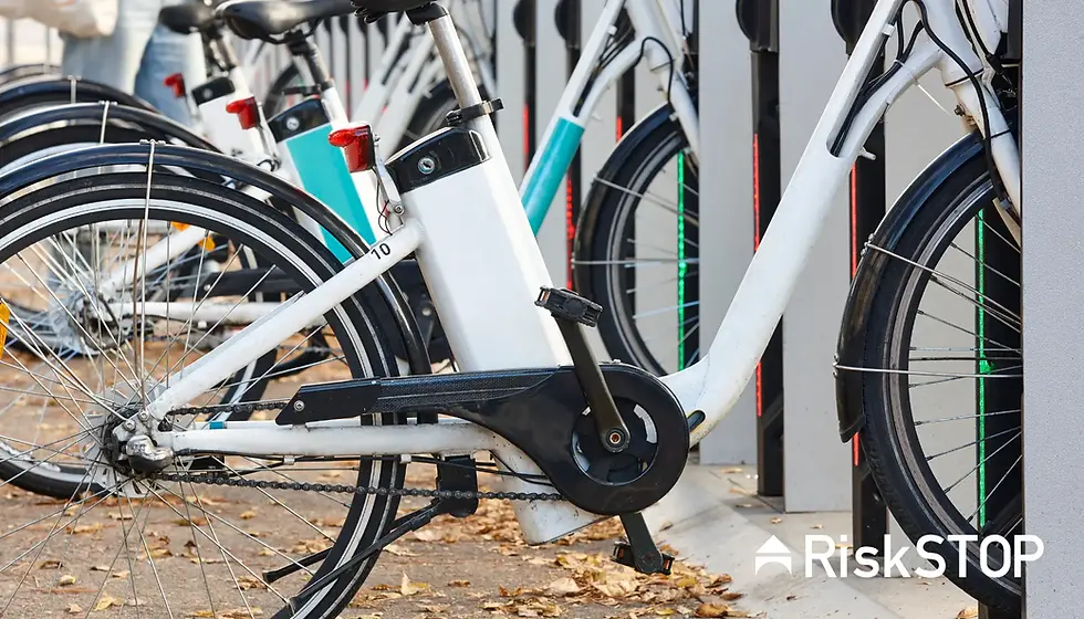 White e-bikes docked at a station, with autumn leaves on the ground. Bright teal accents.