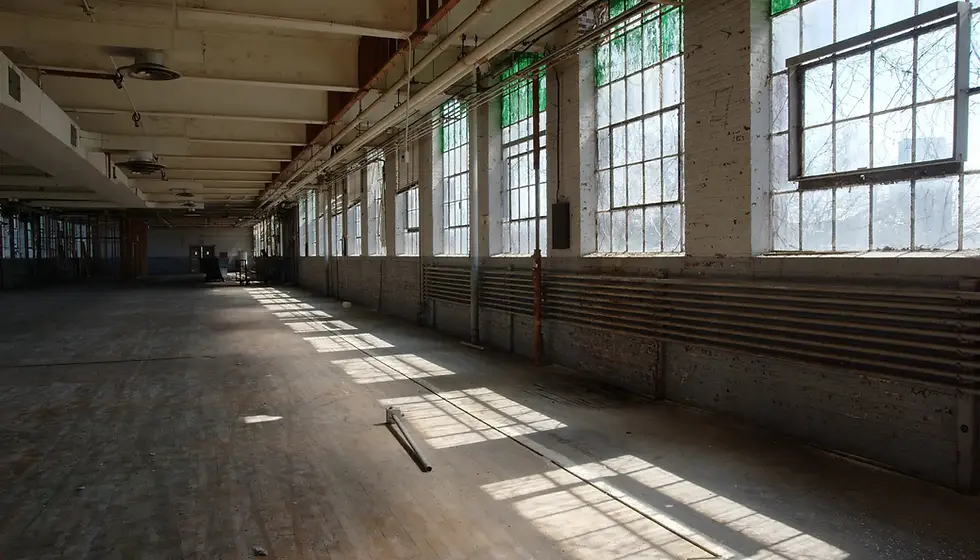 Sunlit empty warehouse interior with large windows casting shadows on the wooden floor. Industrial feel and quiet atmosphere.