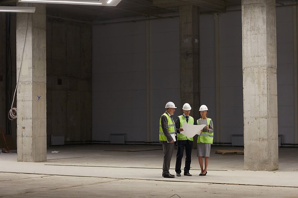 A group of professionals in high-visibility jackets and hard hats reviewing blueprints inside an unfinished building, symbolising collaboration and focusing on the bigger picture in risk management planning